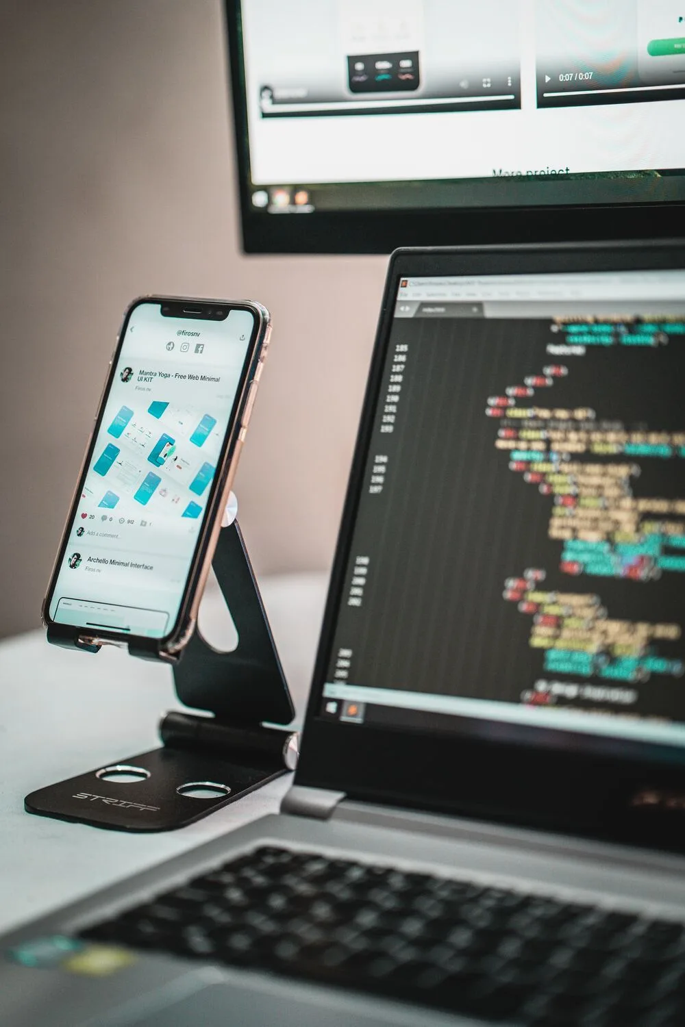 Smartphone mit App neben Bildschirm mit Quellcode – App- und Web-Entwicklung