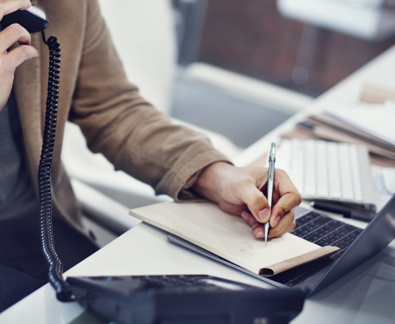 Person taking notes during a phone call next to a laptop — contact appfarms